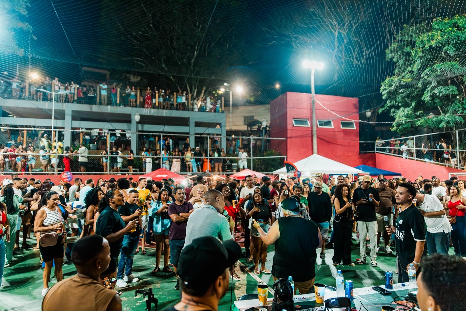 Artistas cantam de frente para a plateia, que acompanha de perto; moradores assistem também do alto da arquibancada